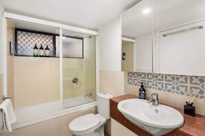 A bathroom with a glass-enclosed shower, a toilet, a sink, and a mirror. - Galleries Apartments, 1 Bed, Parking, Balcony (Fortitude Valley)