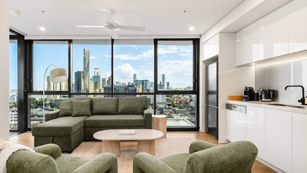 Un salón moderno con un sofá modular, una mesa de centro redonda y vistas a la ciudad a través de amplios ventanales.