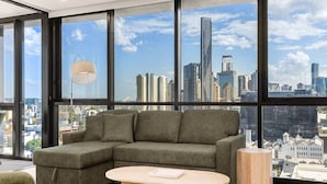 Una sala de estar moderna con un sofá modular, una mesa de centro redonda y grandes ventanales con vistas al horizonte de la ciudad.