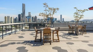 Terraza en la azotea con vistas al horizonte de la ciudad, mobiliario exterior y plantas en macetas.