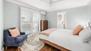 Ein Schlafzimmer mit einem Bett, einem Sessel, einem Schminktisch, einem Schrank und einem Deckenventilator.