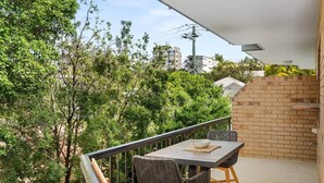 Ein Balkon mit Tisch und Stühlen, eine Backsteinmauer und Bäume im Hintergrund.