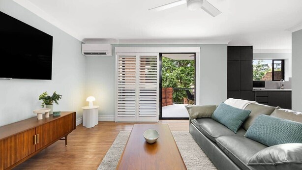 Ein modernes Wohnzimmer mit einer Couch, einem Couchtisch, einem Fernseher und einer Glastür zum Balkon.