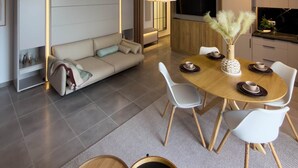 En moderne stue med sofa, spisebord, stole, et køkken og store hængende lamper.
