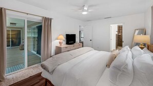 Habitación de hotel con una cama, televisor, escritorio con lámpara, puerta corrediza de vidrio a un balcón y ventilador de techo.