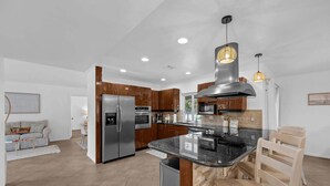 Una cocina moderna con electrodomésticos de acero inoxidable, armarios de madera, encimera de granito e iluminación colgante.