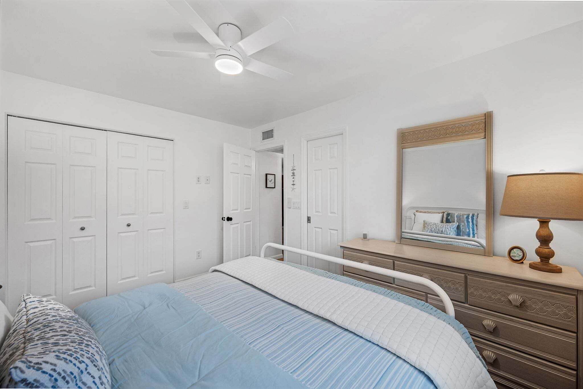 A bedroom with a bed, dresser, mirror, and ceiling fan.