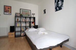 Un dormitorio con una cama, una estantería, un radiador y un cuadro en la pared.