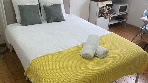 A neatly made bed with a yellow blanket, a small desk with a microwave, and a chair in a room with wooden flooring. - La Folie Urban Studio R Publique Marais Canal St Martin (Paris)