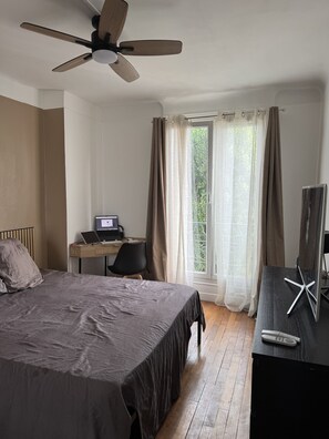 A bedroom with a bed, a desk with a laptop, a TV, and a ceiling fan. - Charmant 2 pi ces Proche a Roport Paris Direct via la Ligne 14 (Orly)
