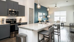 A modern kitchen with dark cabinets, a microwave, stove, and a large island with bar stools.
