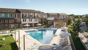 A residential building with a swimming pool, outdoor seating, and a green lawn.