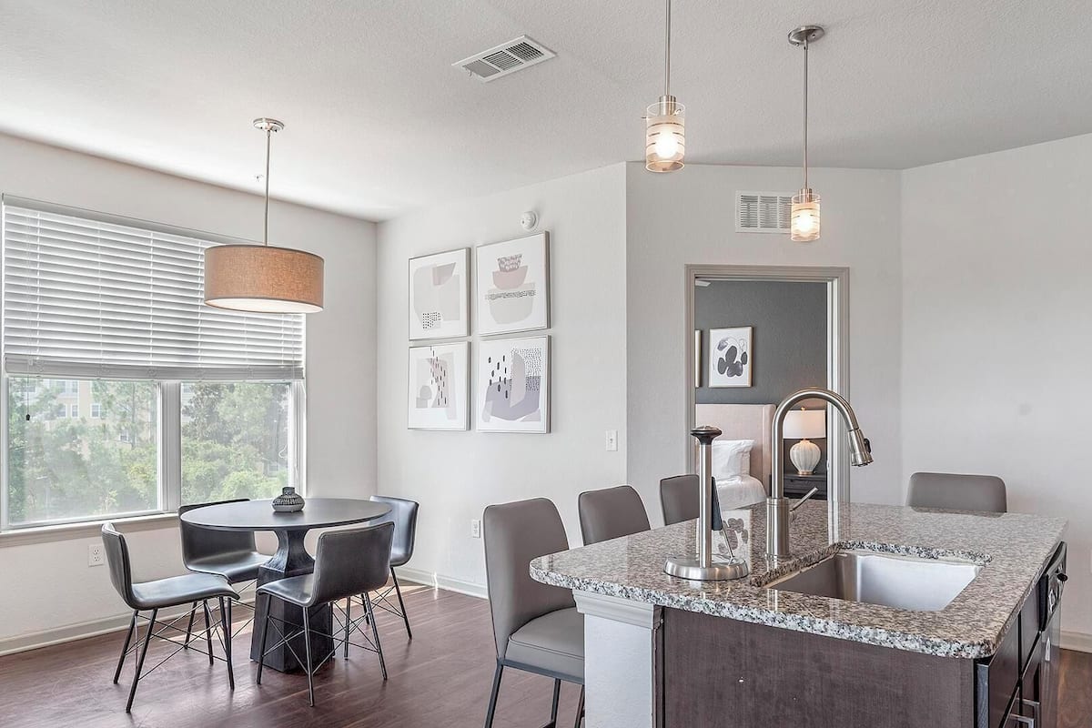A modern kitchen with a granite countertop, stainless steel sink, and pendant lighting.