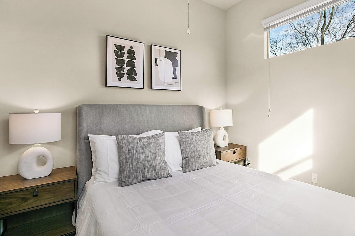 A bedroom with a bed, two bedside tables, a window, and two framed pictures on the wall.