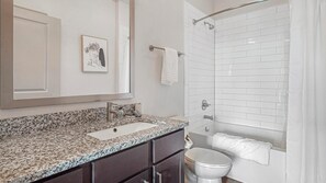 A bathroom with a granite countertop, a white sink, a toilet, and a shower with white tiles. - Landing Apartments near Gateway Crossing (McCordsville)