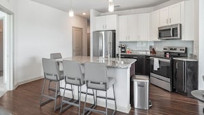 A modern kitchen with white cabinets, stainless steel appliances, and a granite countertop. - Landing Apartments near Gateway Crossing (McCordsville)