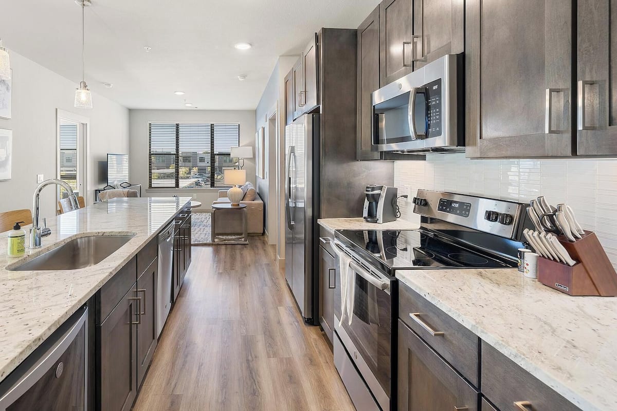 A modern kitchen with a central island, stainless steel appliances, and a view to the living area.