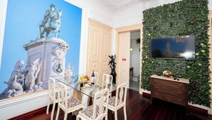 Ein Essbereich mit einem Glastisch, weißen Stühlen, einem großen Wandgemälde, einem Fernseher und einer begrünten Wand.