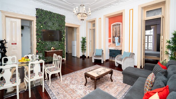 Ein geräumiges Wohnzimmer mit einer Chandelüster, einem Fernseher, einer Essecke mit Stühlen und einem Tisch sowie einem Sofa mit Kissen.