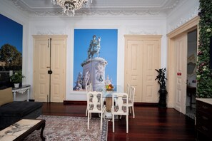 Ein Zimmer mit Esstisch, Stühlen, einer Couch, einer Kandelaber und einem großen Gemälde.