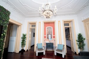 Ein Zimmer mit einer Chandelüster, zwei Sesseln, einem kleinen Tisch und einem Kamin.