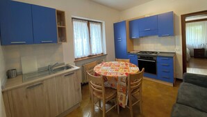 Una cocina compacta con armarios azules, una mesa de comedor con mantel estampado y un sofá en la sala.