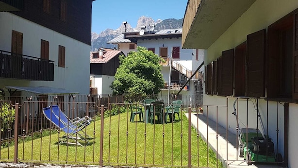 Un patio con césped, un árbol y una silla de jardín verde.