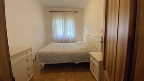 Un dormitorio con cama, mesita de noche, cómoda y puerta de madera.