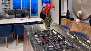 A modern kitchen with a central island, a dining area with a sofa and chairs, and a large window with a view. - Oceana Luxury Escape | 3BR/3BA | Ocean Views (Bucerias)