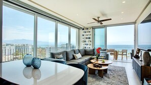 A spacious living area with a large sofa, a dining table, and a balcony with a view of the city and the sea. - Oceana Luxury Escape | 3BR/3BA | Ocean Views (Bucerias)