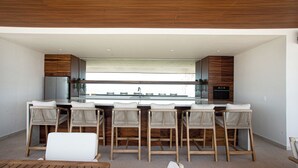 A modern kitchen with a central island, bar stools, and a view to the outside. - Oceana Luxury Escape | 3BR/3BA | Ocean Views (Bucerias)