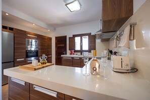 A modern kitchen with wooden cabinets, a built-in oven, a countertop with a bottle and glasses, and a toaster. - Casa Victoria | Ibiza town 5 min (Islas Baleares)