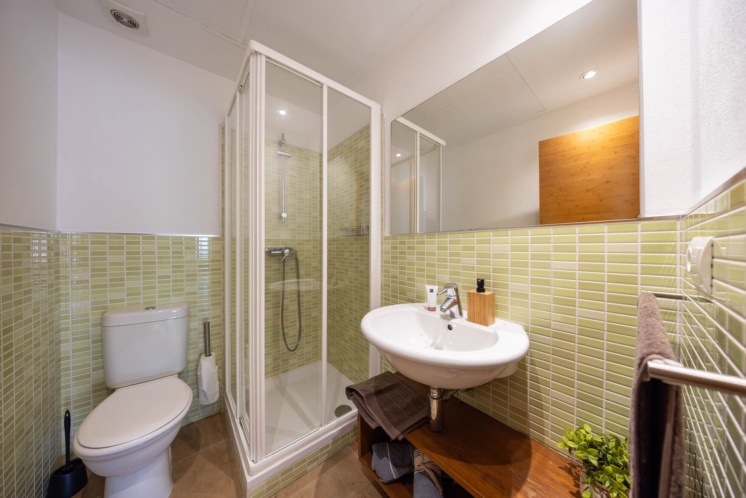 A bathroom with a toilet, shower, sink, and a mirror.