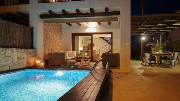 Ein Swimmingpool mit Holzterrasse, einer Steinmauer und einer Sitzgelegenheit mit Stühlen und einem Tisch.