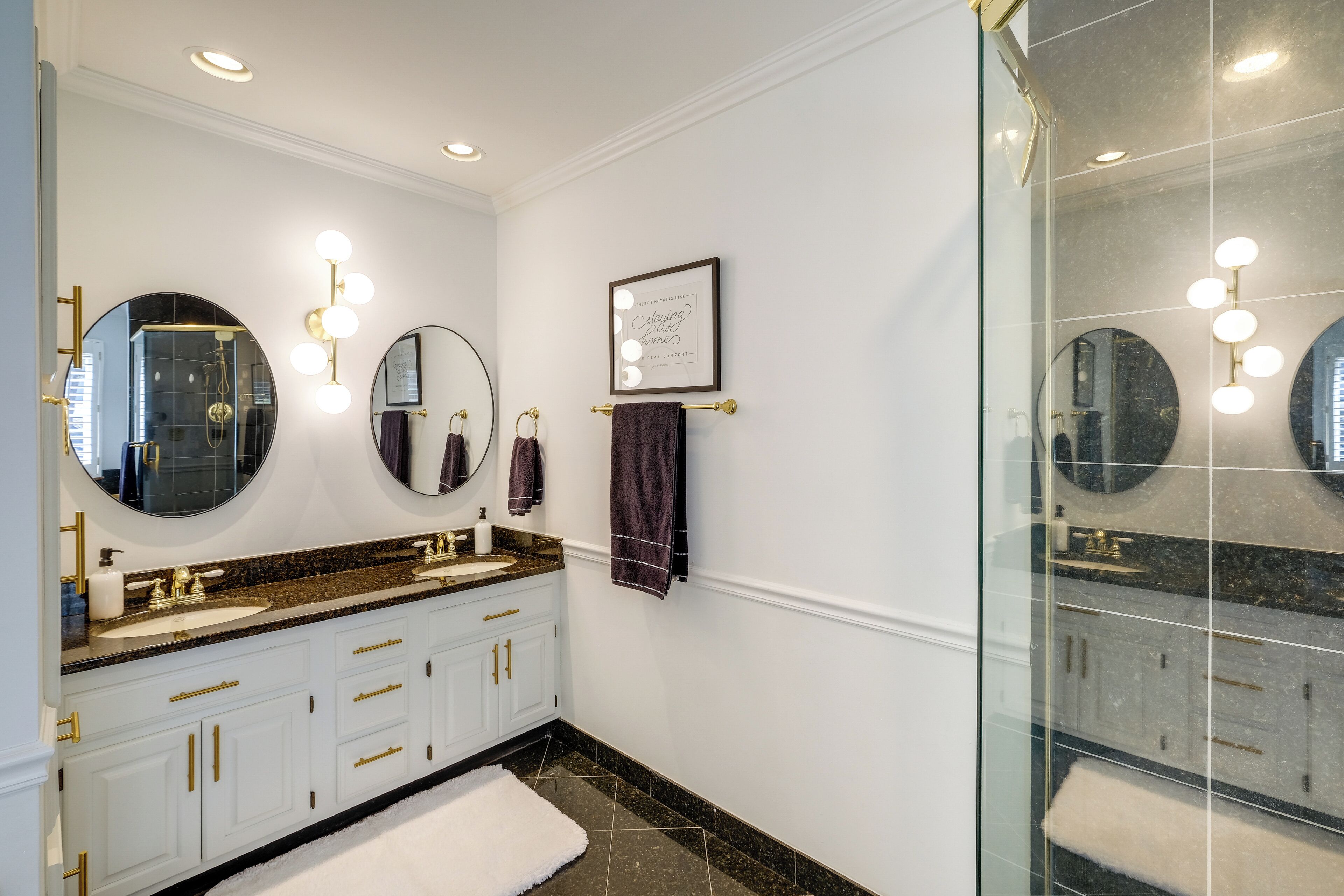 A bathroom with two sinks, a large mirror, wall sconces, and a framed quote.