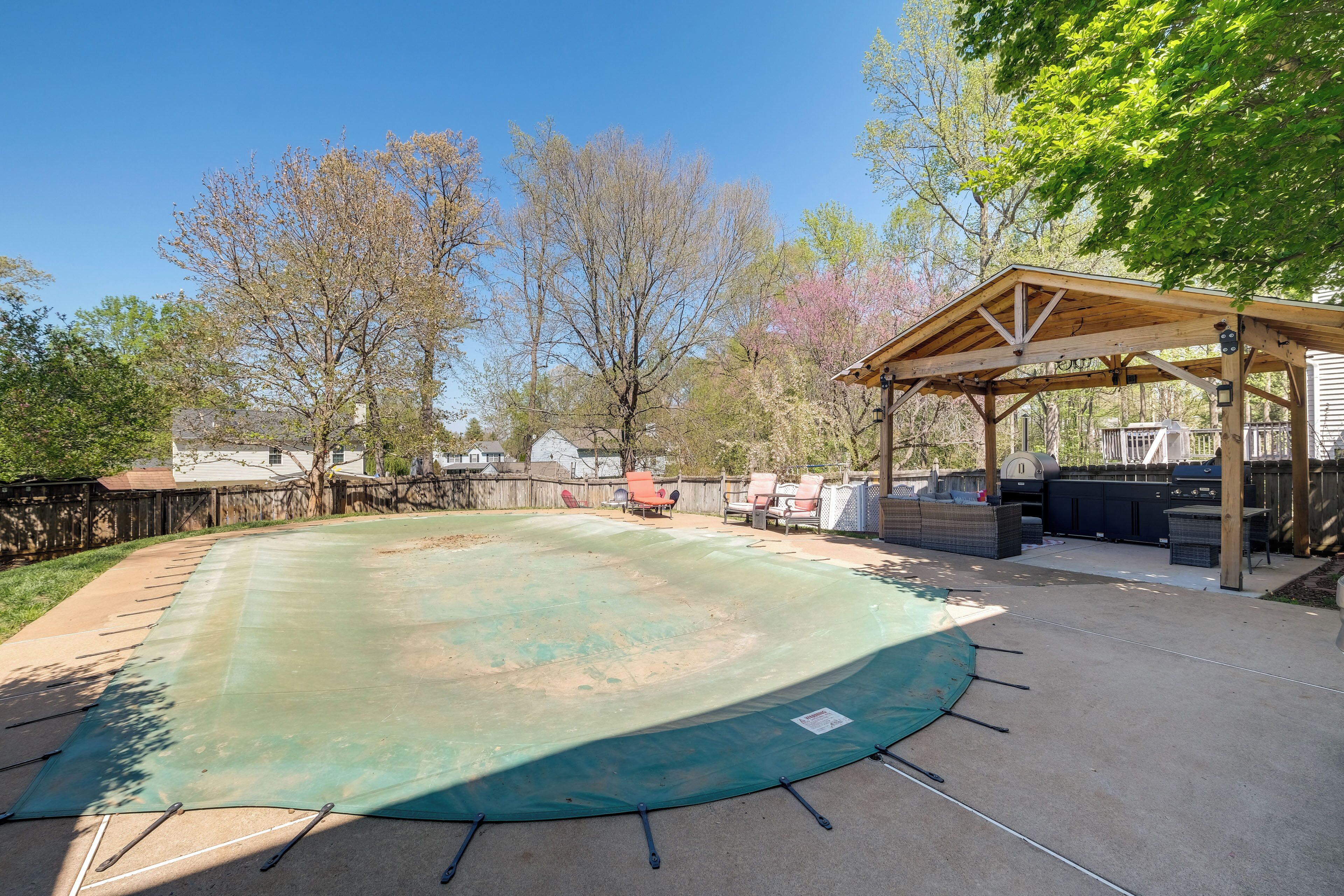Ein Garten mit überdachtem Pool, Grillplatz und einer Holzpergola.