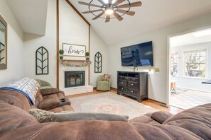 A living room with a fireplace, a television, a sofa, and a ceiling fan.