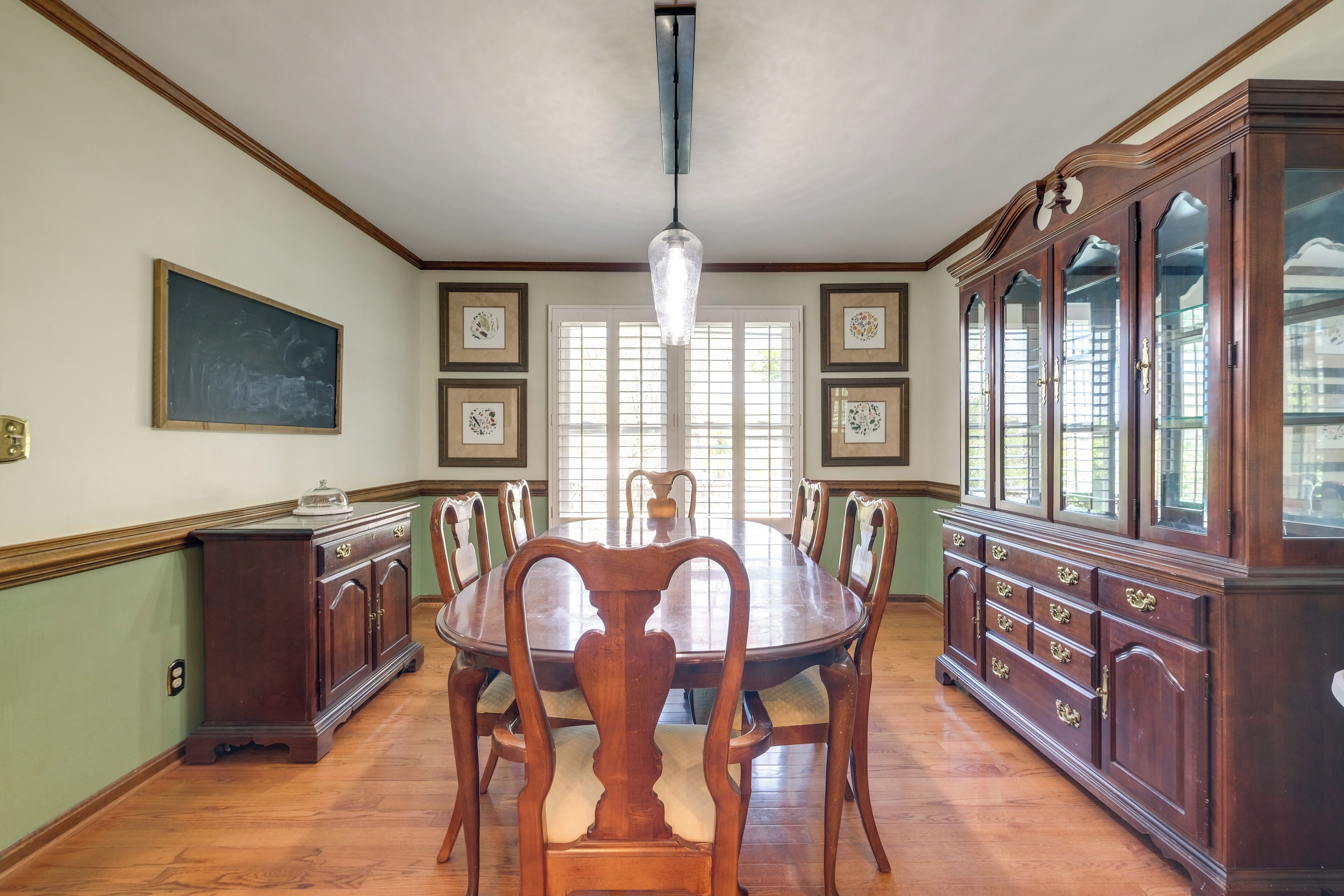 A dining room with a wooden table, chairs, a chandelier, and a large wooden cabinet with glass doors.