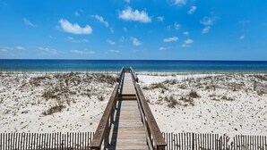Ein hölzerner Steg führt zu einem Strand bei strahlendem Himmel.