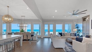 Ein geräumiger Wohnbereich mit großem Fenster zum Meer, Deckenventilator und einer Bar mit Hockern.