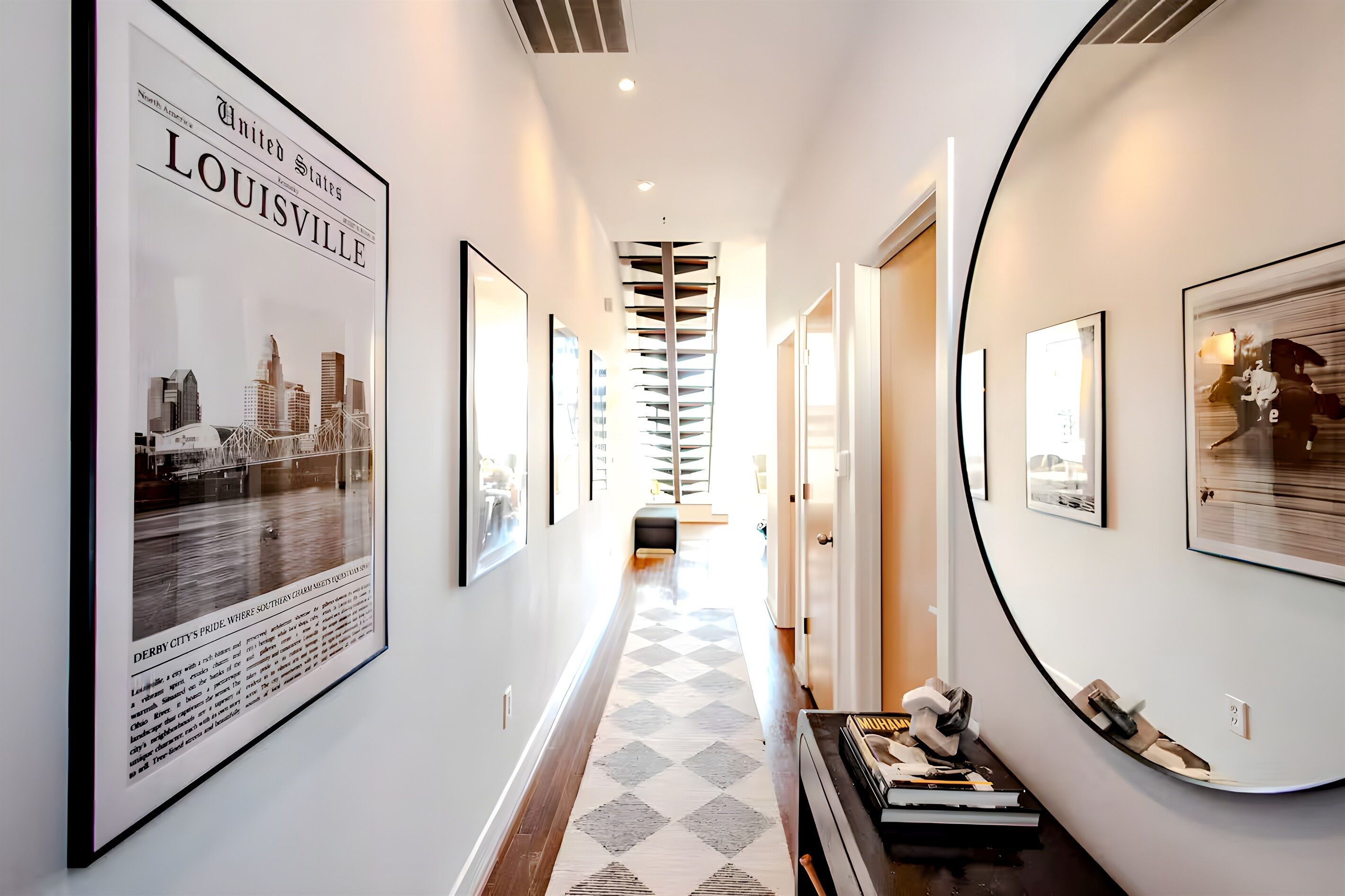 Walk through this stylish hallway featuring a bold checkerboard runner and a collection of stunning local photography. The giant round mirror at the end is perfect for one last outfit check before heading out.