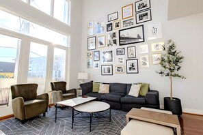 Cozy up in this massive charcoal sofa surrounded by an incredible gallery of framed memories. The olive green armchairs and sleek round coffee tables make this the ultimate spot for group chats. - Gorgeous NuLu Retreat | Gated Parking | Two Patios (Louisville)