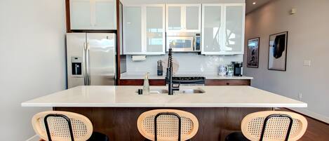 Pull up a stylish black and cane stool to the expansive kitchen island for a casual breakfast. The sleek white countertops provide plenty of room for meal prep or evening cocktails.