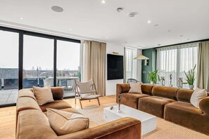 A modern living room with a large window, a sofa set, a coffee table, and a television. - Modern 2-Bedroom Condo (London)