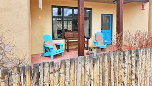 En overdækket terrasse med to blå stole, et træbord og en blå dør.