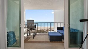 Un balcon avec vue sur la plage, une chaise, un canapé et une valise.