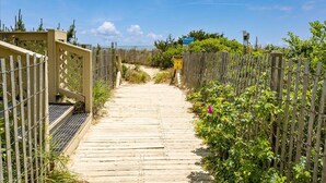 Un sentier en bois mène à une plage, bordé de clôtures en bois et de verdure.