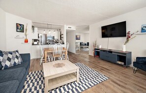 A modern living room with a sofa, coffee table, TV, and dining area.