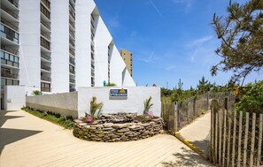 A modern hotel with a prominent pyramid-shaped structure, a stone pathway, and a wooden fence. - Beachfront 1 BR 1.5 BA Unit with a Pool and Fantastic Ocean Views! (Ocean City)