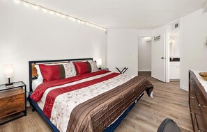 A bedroom with a bed, bedside tables, a nightstand, a dresser, and a door leading to a bathroom. - Beachfront 1 BR 1.5 BA Unit with a Pool and Fantastic Ocean Views! (Ocean City)
